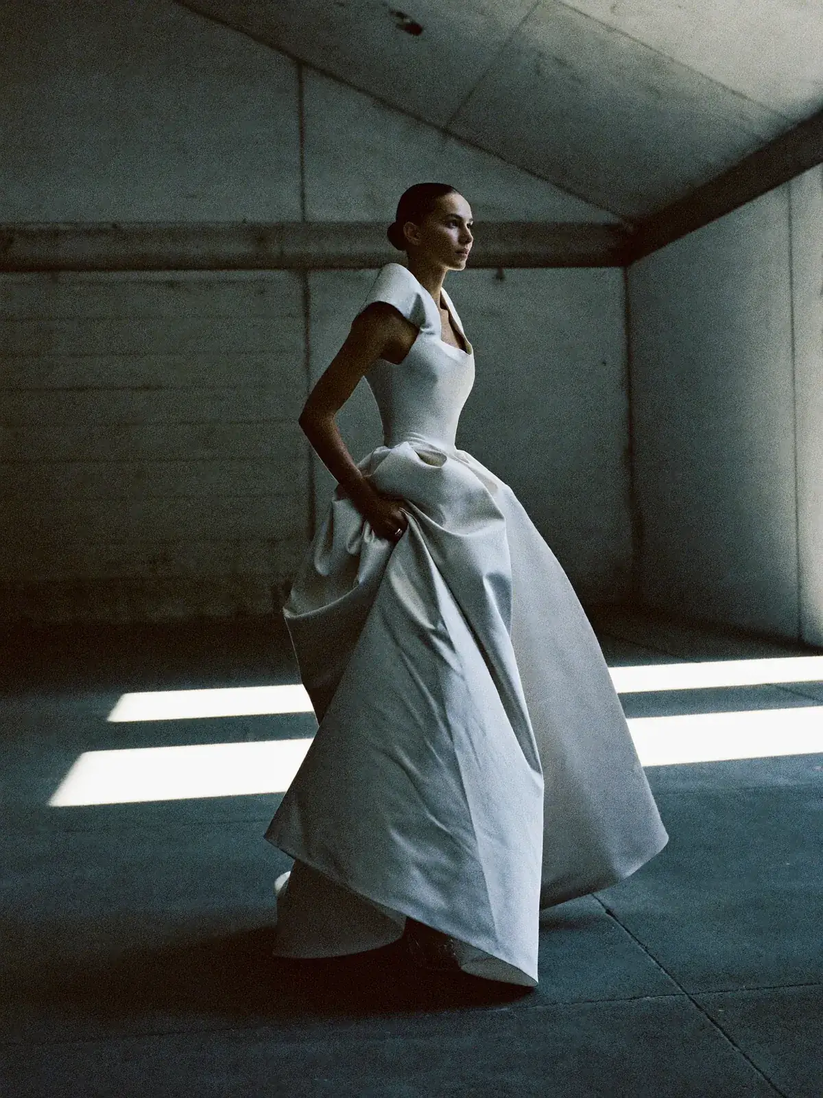 Bride in a sculptural silk mikado gown with a structured shoulder, in a concrete hall