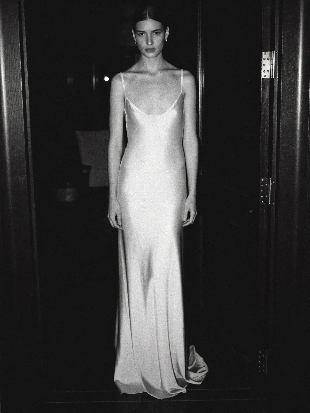 Bride in a bias cut silk crepe slip gown standing in a dark doorway
