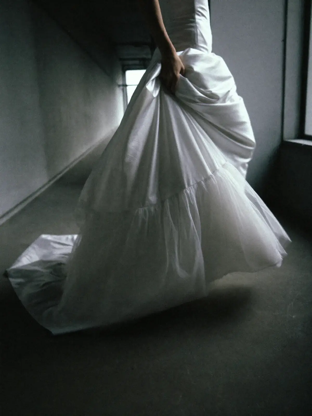 Bride running through a concrete corridor, the gathered tulle skirt trailing behind her
